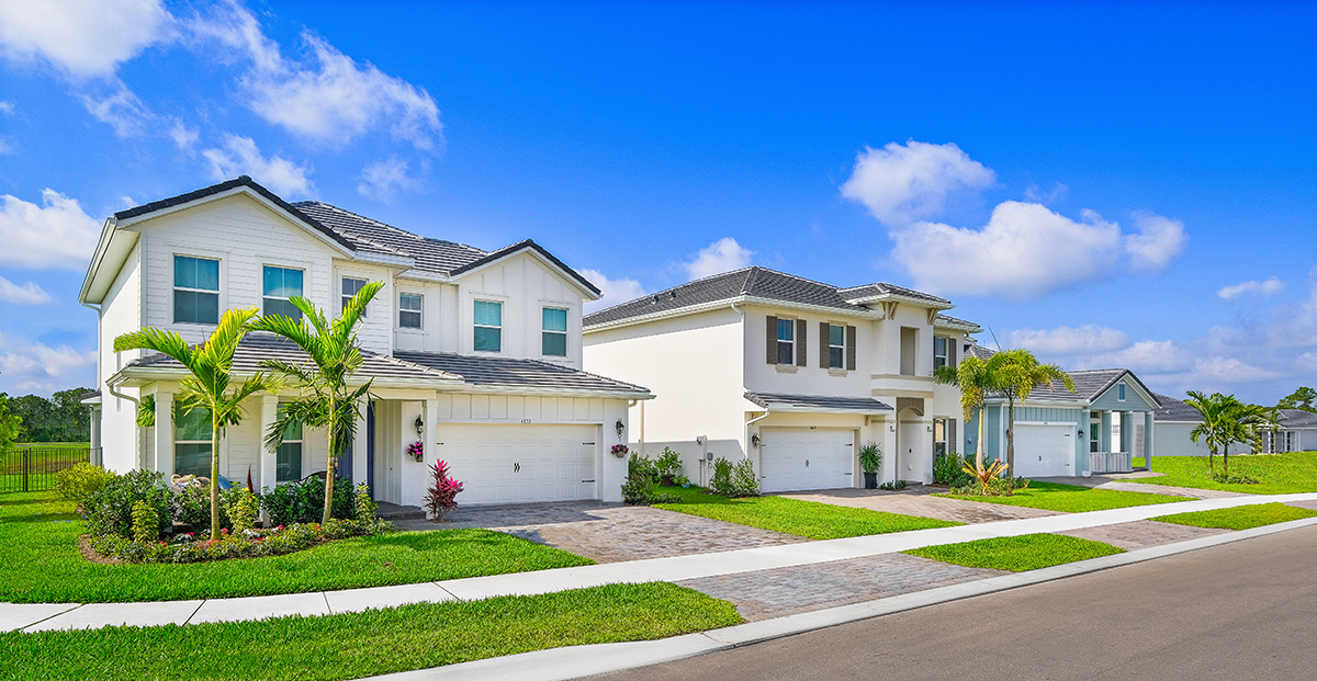 Community of new homes, focused on 2 cream stucco homes with palm trees in front.